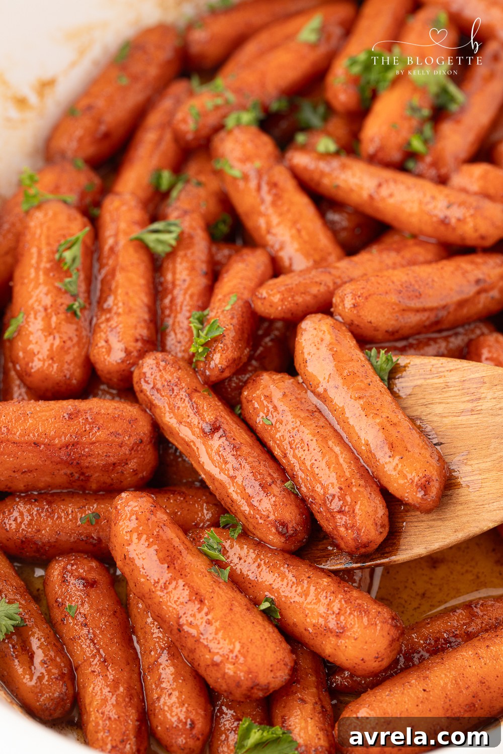 Close-up of golden-brown Honey Roasted Baby Carrots garnished with fresh parsley, in a white serving bowl.