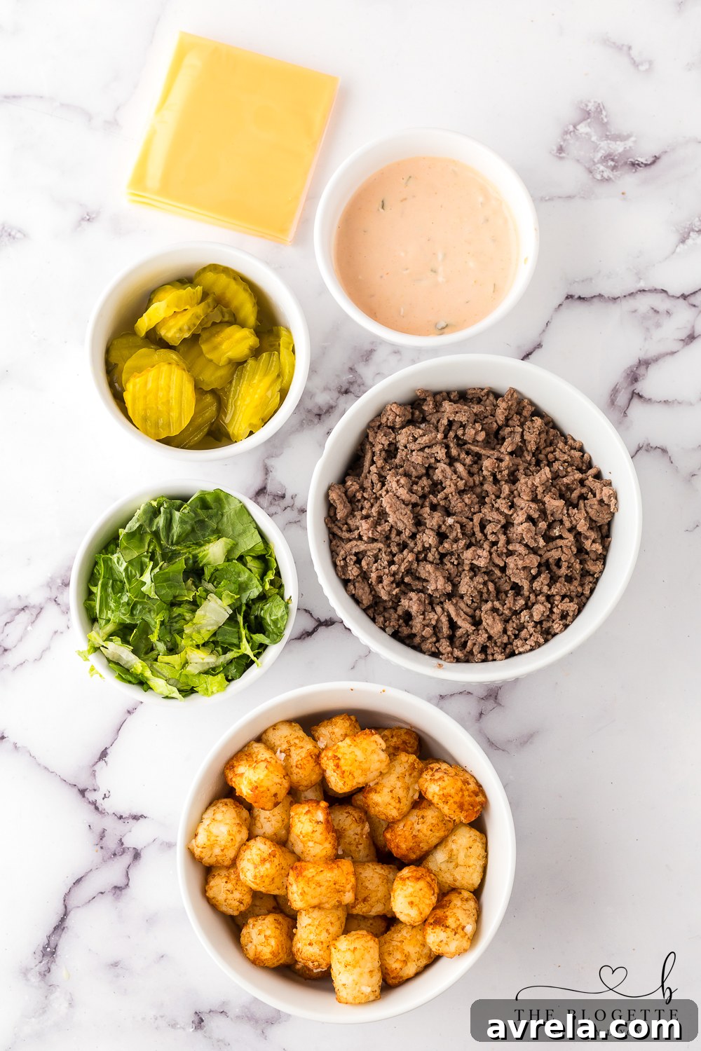 All the fresh ingredients for Cheeseburger Totchos laid out on a table, including cooked ground beef, tater tots, American cheese, and toppings.