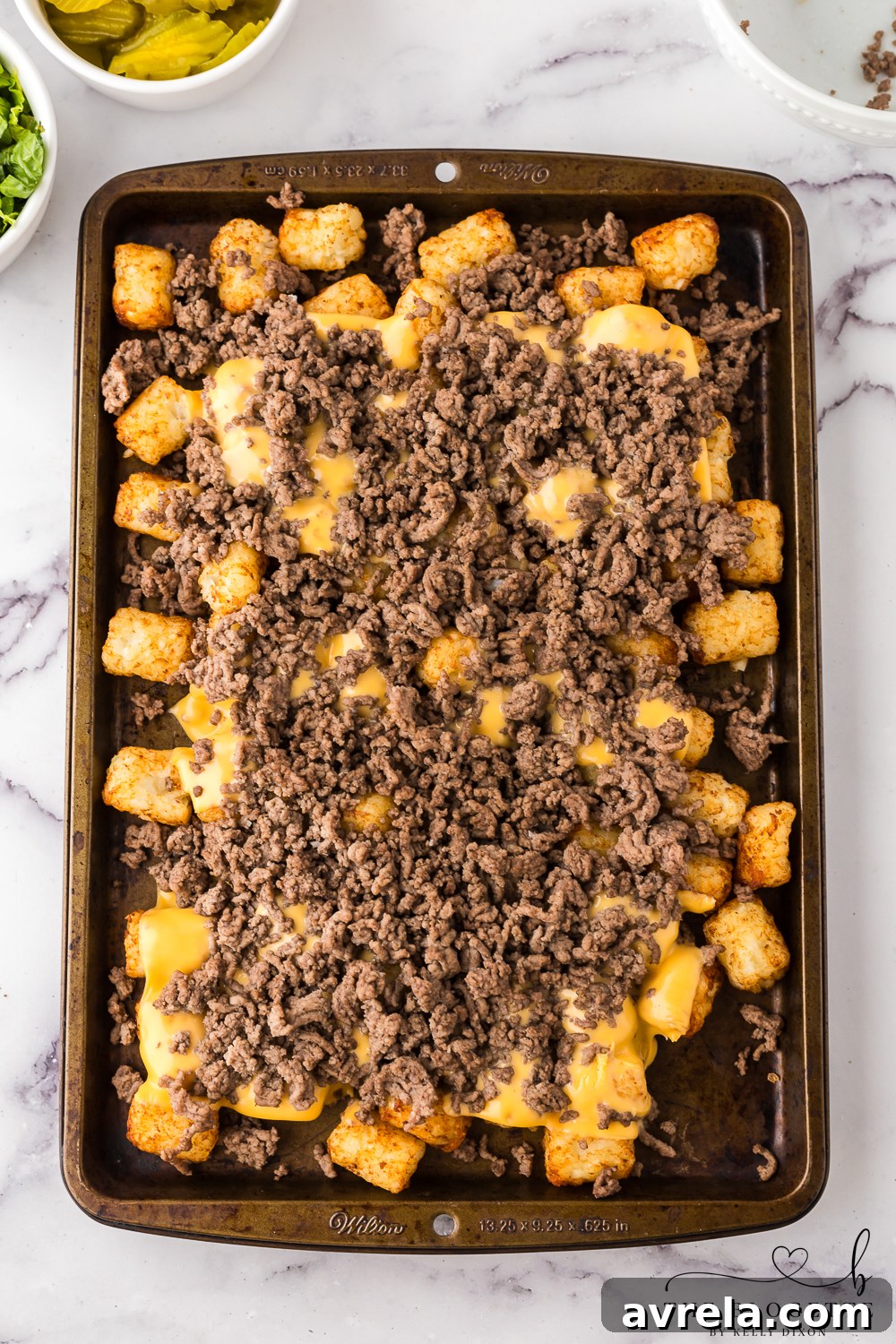 Melted American cheese and ground beef layered over tater tots after broiling, ready for fresh toppings.
