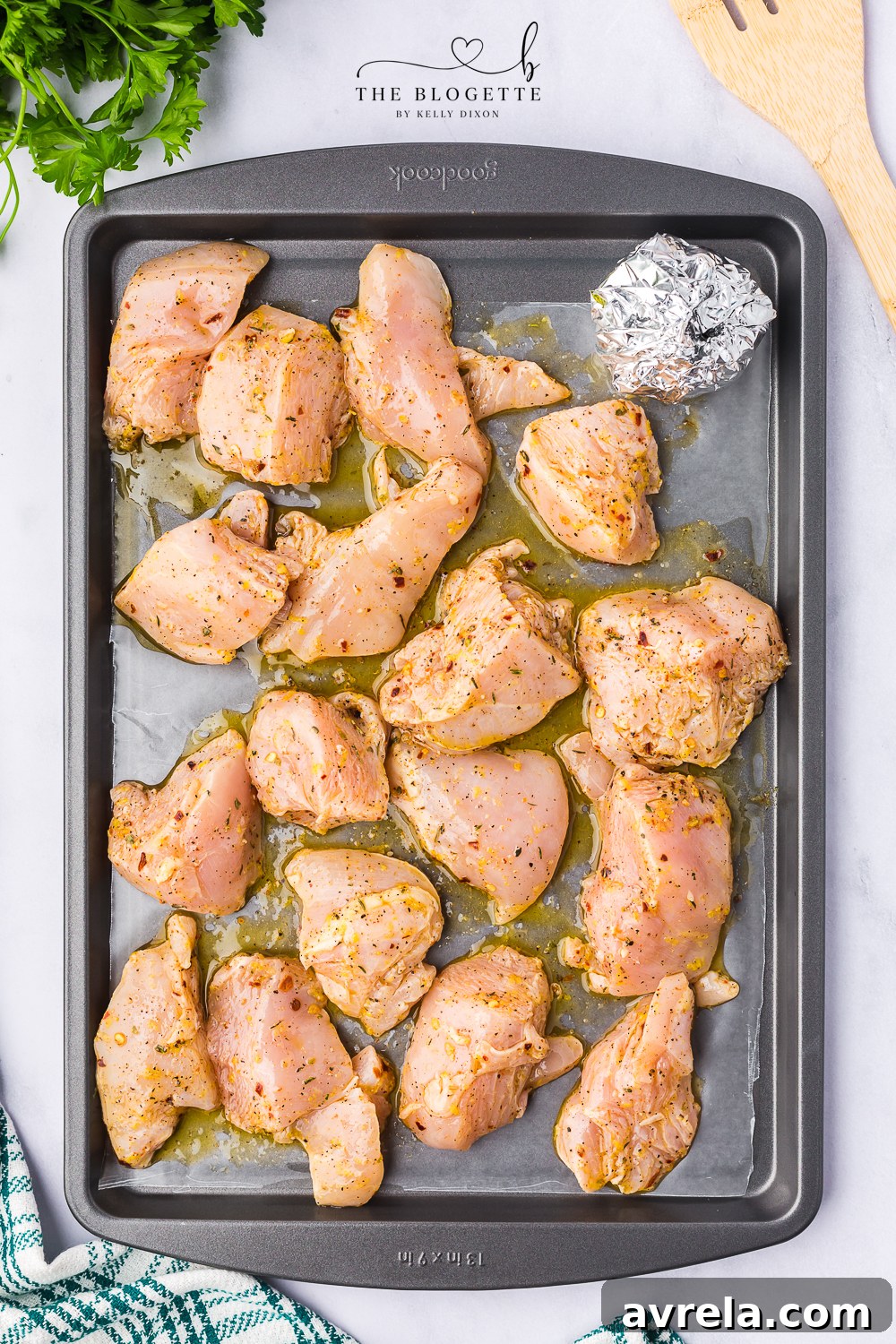 Marinated chicken pieces and a foil-wrapped garlic bulb arranged on a baking sheet, ready to be roasted together in the oven for a delicious meal.