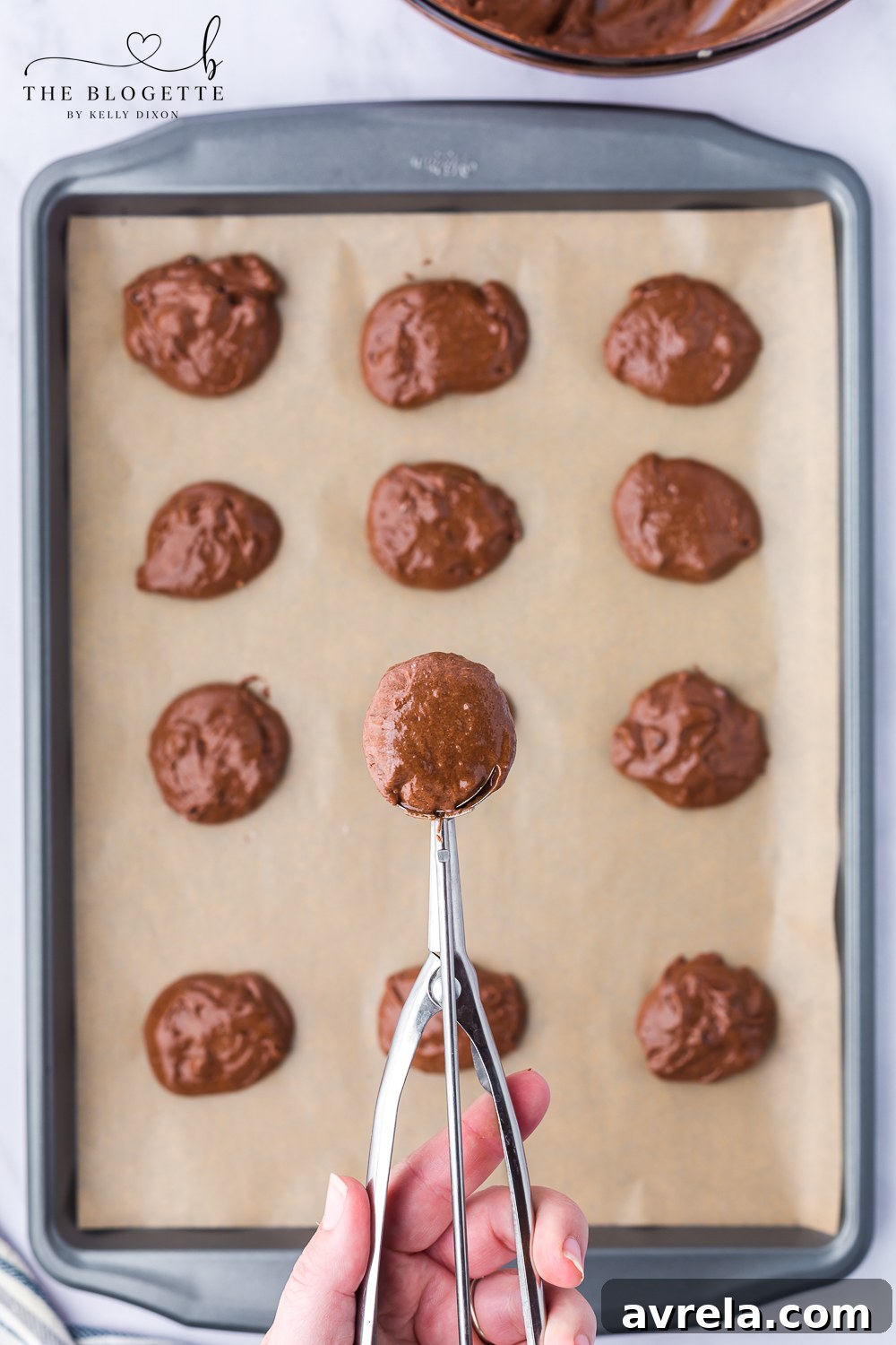 Scooping brownie cookie dough onto a parchment-lined baking tray.