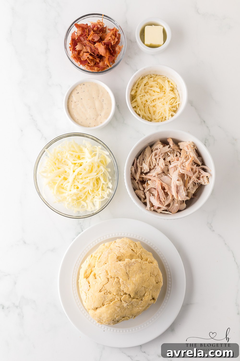 Fresh ingredients laid out for a homemade Costco Chicken Bake, including pizza dough, shredded chicken, cheeses, bacon, and Caesar dressing.