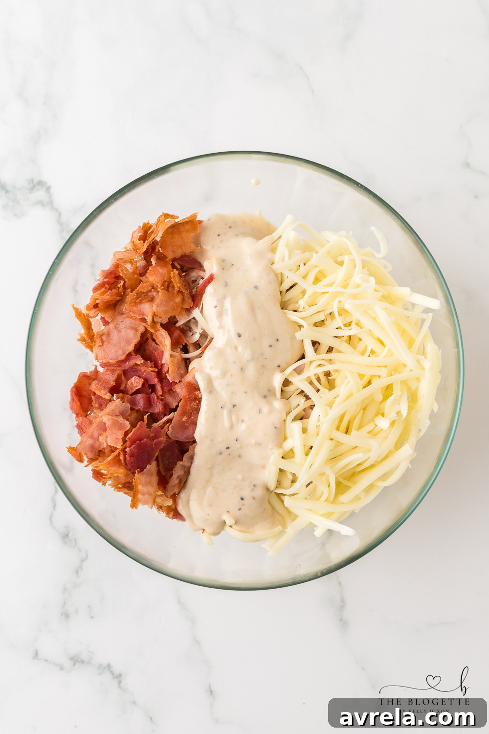 Close-up of the chicken mixture in a bowl, featuring shredded chicken, Caesar dressing, mozzarella, and crumbled bacon.