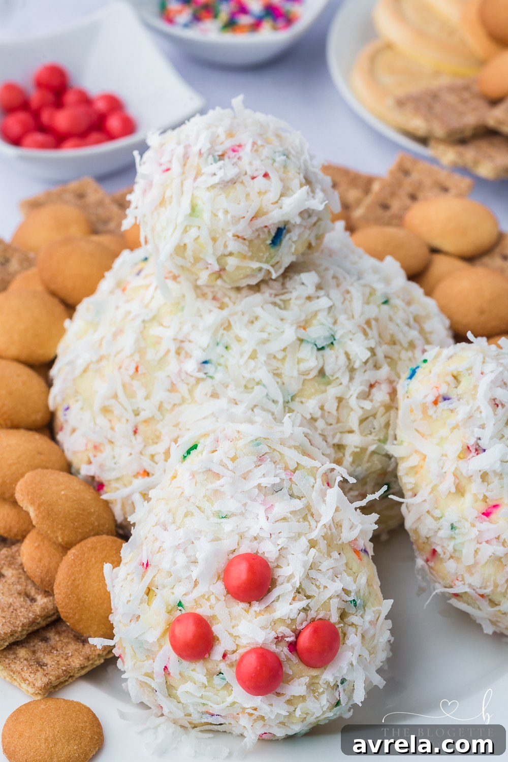 A close-up of the charming Bunny Butt Cheeseball, showcasing its fluffy shredded coconut exterior and delicate pink Skittle toes on a white platter.
