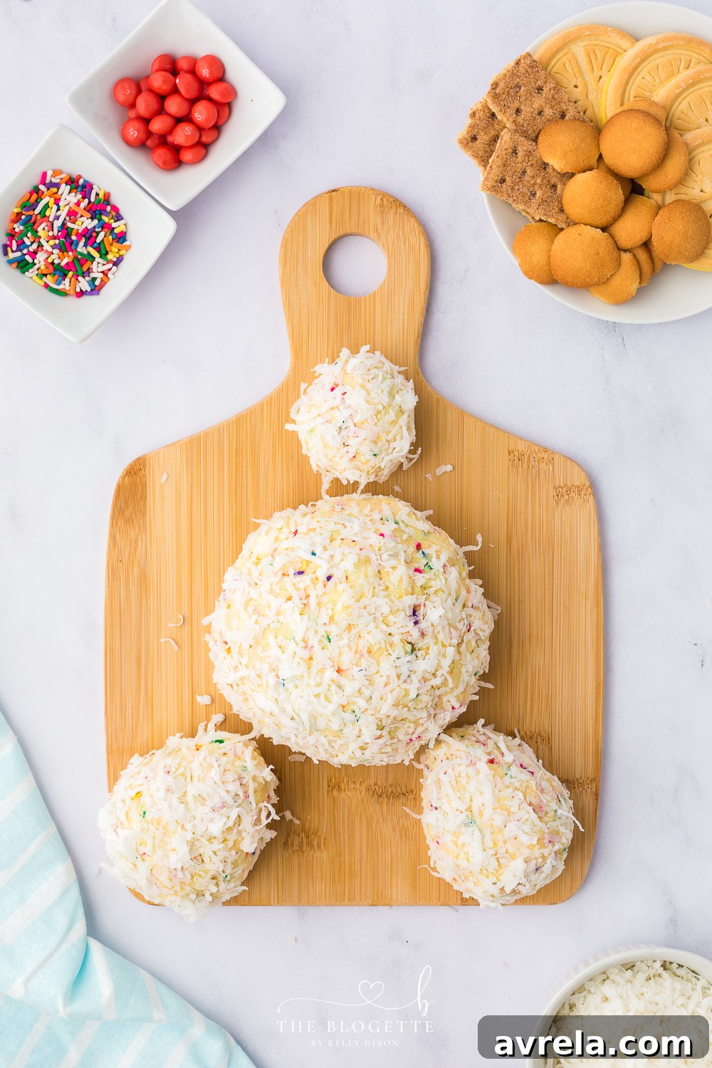Assembling the Bunny Butt Cheeseball by carefully attaching the coconut-coated paws and tail to the main body on a serving platter.