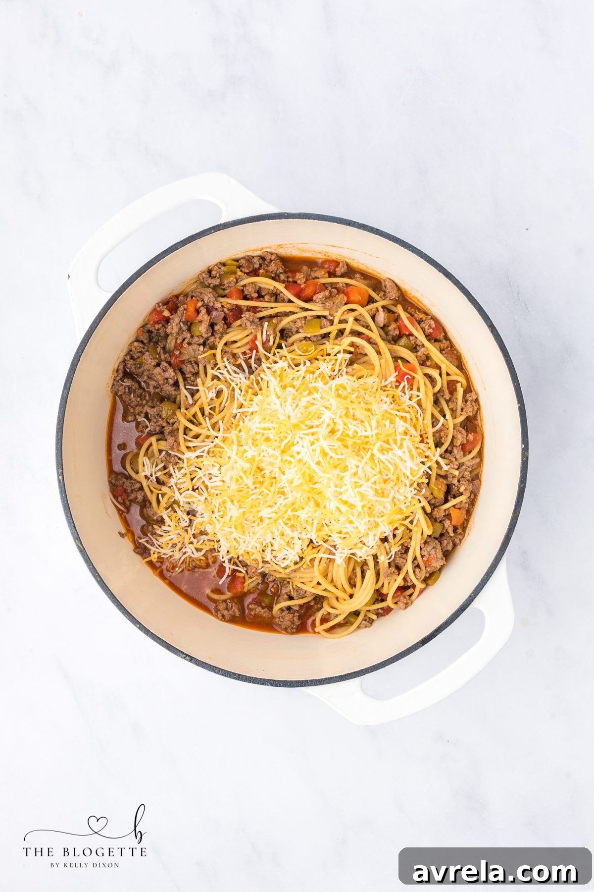Stirring shredded cheese into hot taco spaghetti until melted and creamy.
