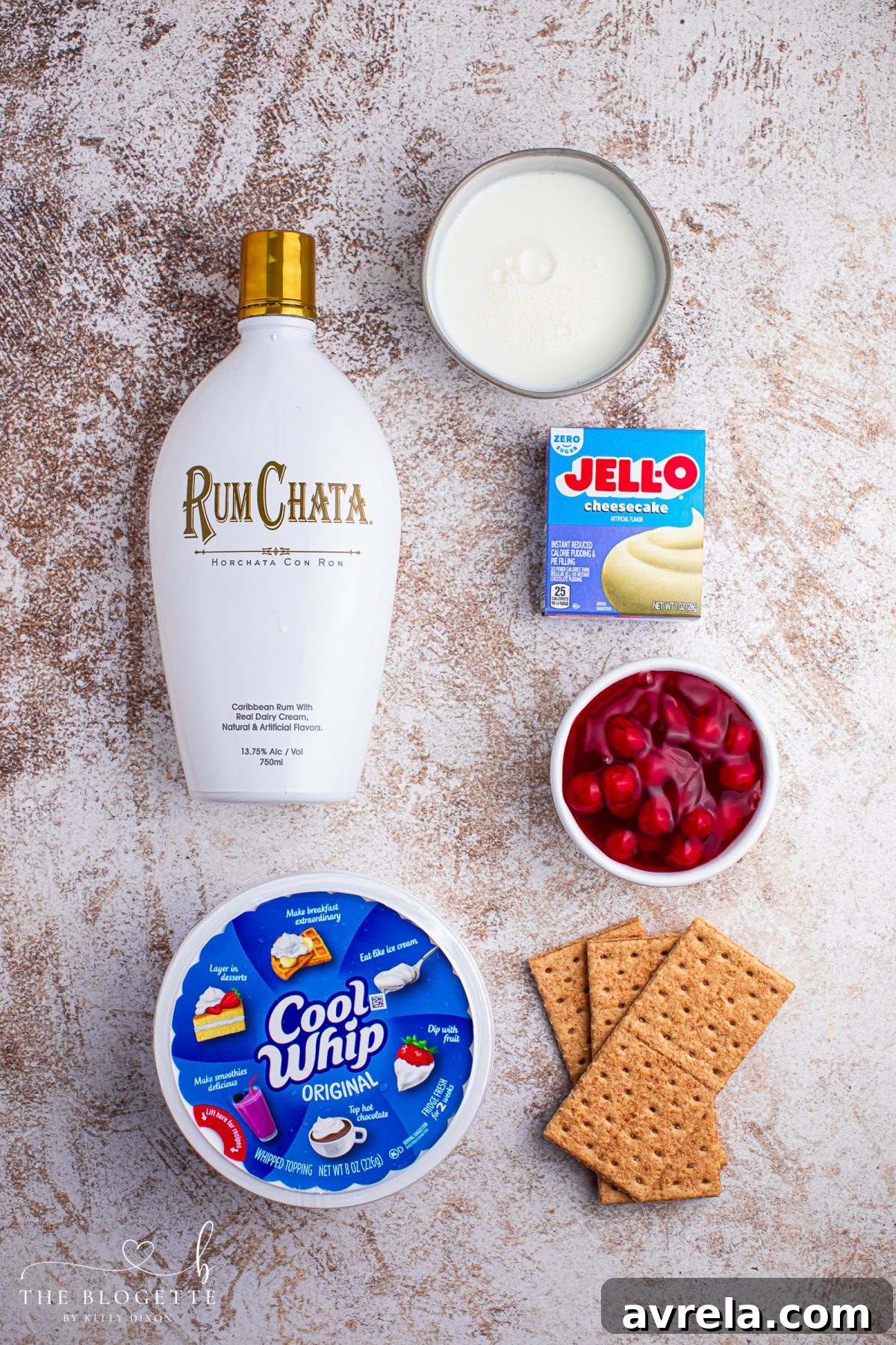 A selection of ingredients laid out, including cheesecake pudding mix, milk, RumChata, Cool Whip, graham crackers, and cherry pie filling, ready for making Cherry Cheesecake Shots.