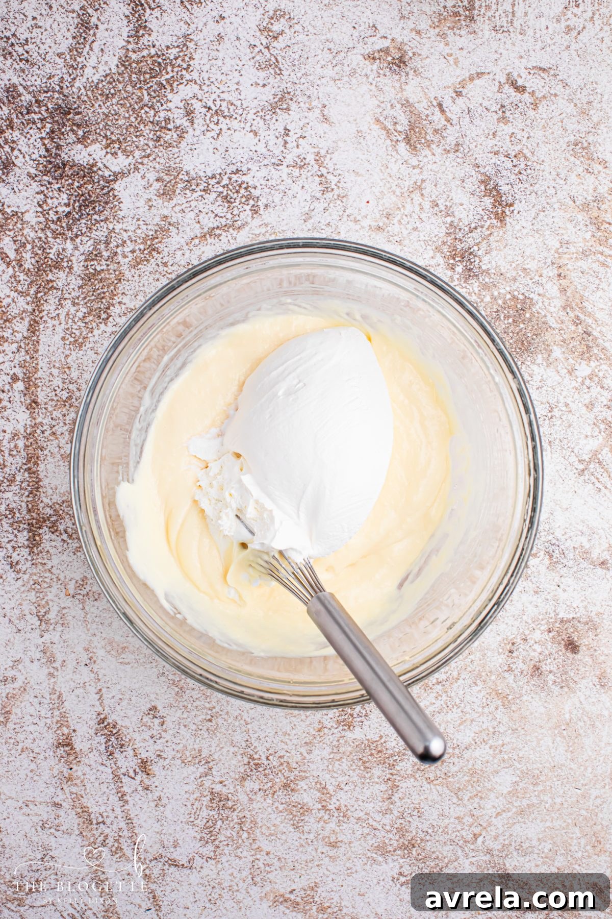 Gently folding in half of the thawed Cool Whip into the cheesecake pudding mixture to create a light and fluffy mousse.