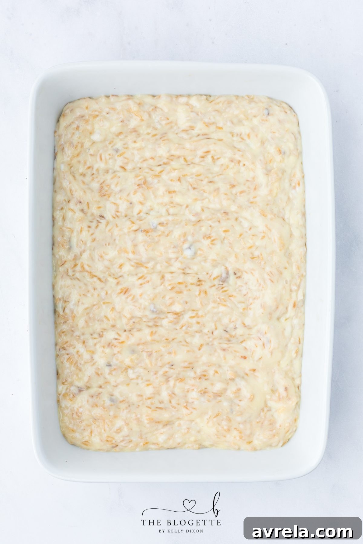 Spreading the creamy rice base evenly across the bottom of a 9x13 baking dish for Forgotten Chicken Casserole.