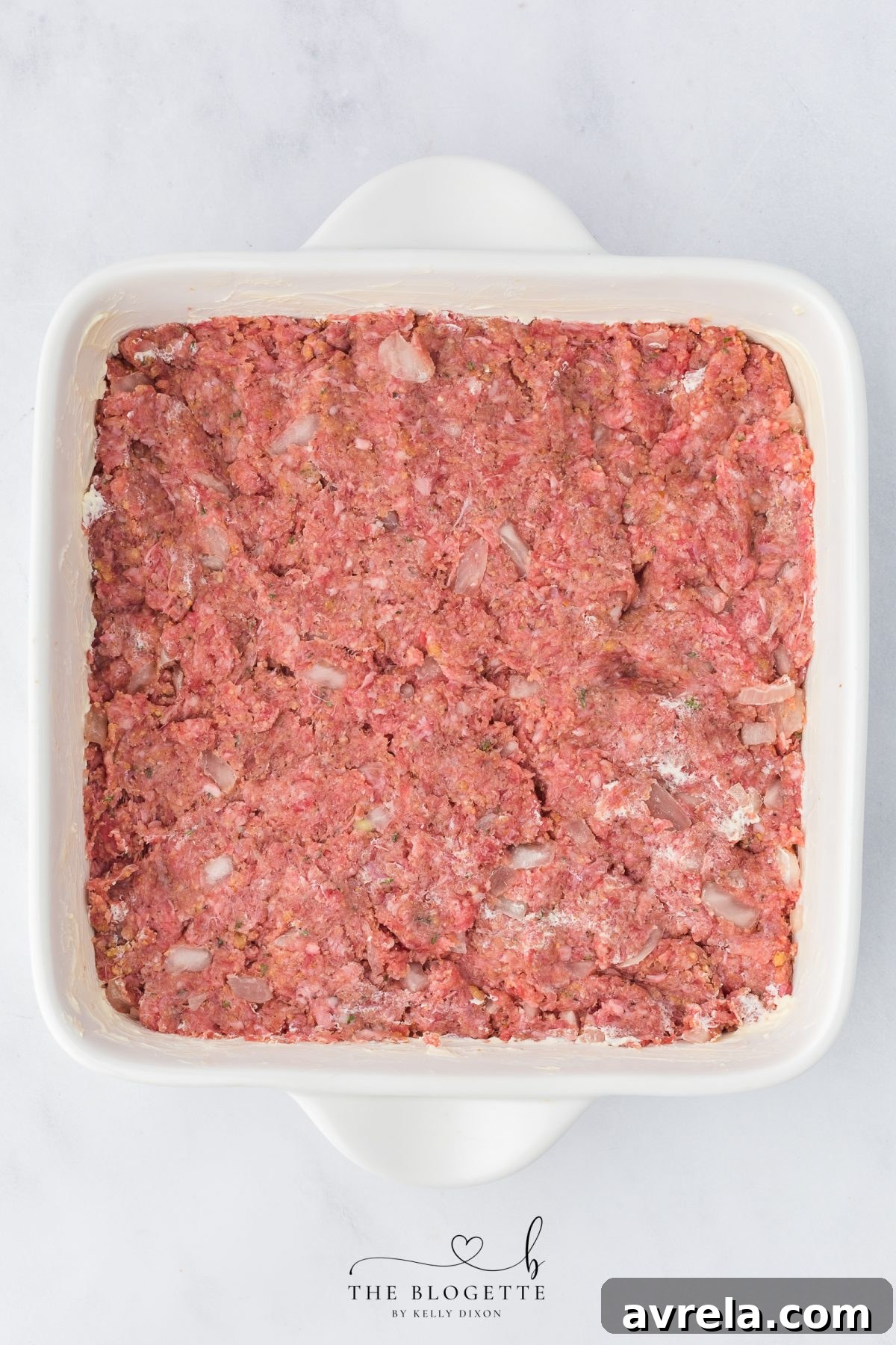 The perfectly spread meatloaf mixture forming the base layer in the baking dish.