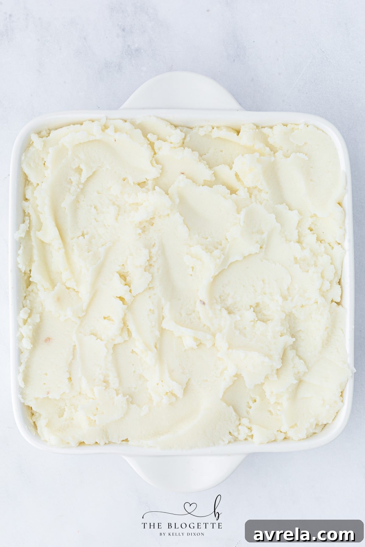 Smoothly layering creamy mashed potatoes over the meatloaf base, ensuring full coverage.