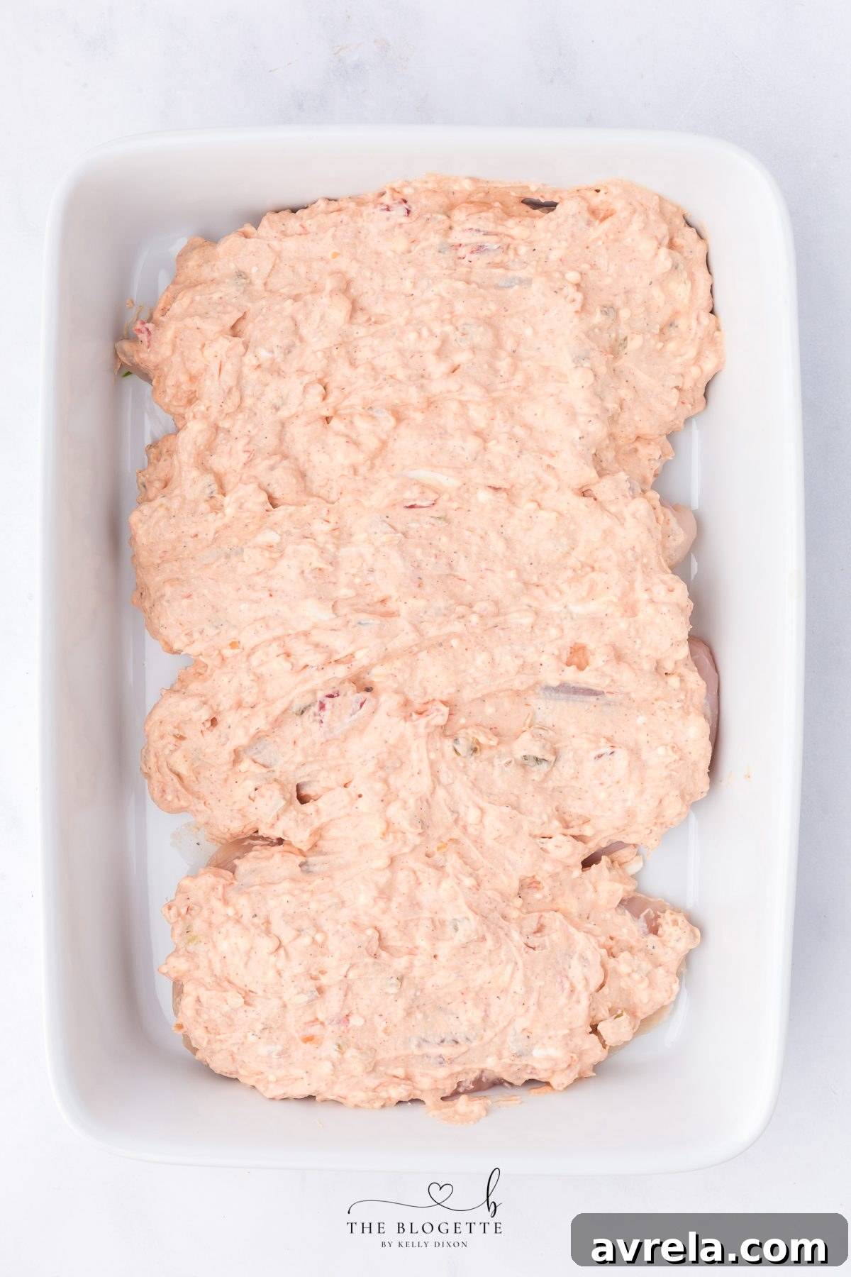 Creamy fajita sauce being spread evenly over the chicken in the casserole dish.