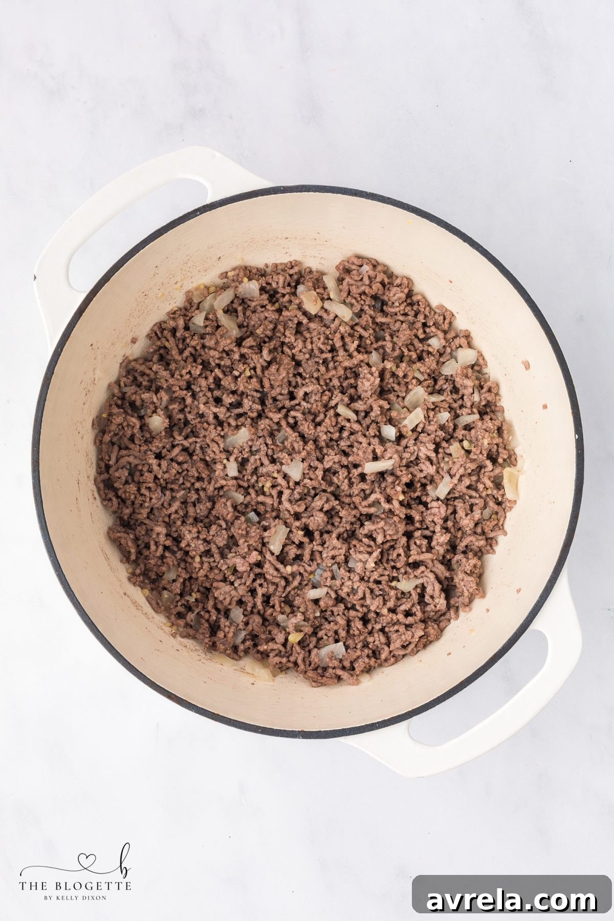 Adding diced sweet onion to the browned ground beef in the pot.