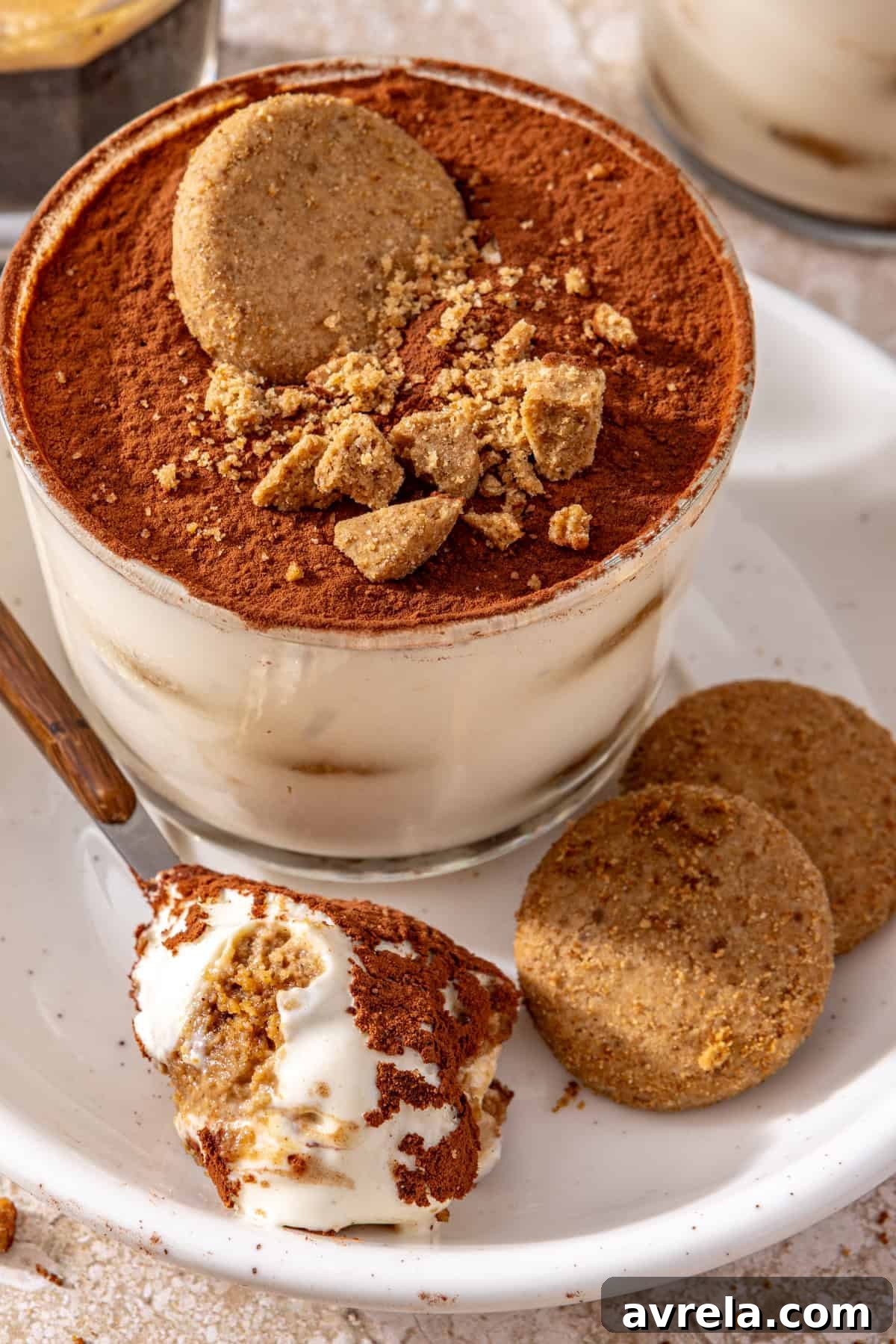 High-protein tiramisu cups served on a plate with cookies and a spoonful of creamy tiramisu