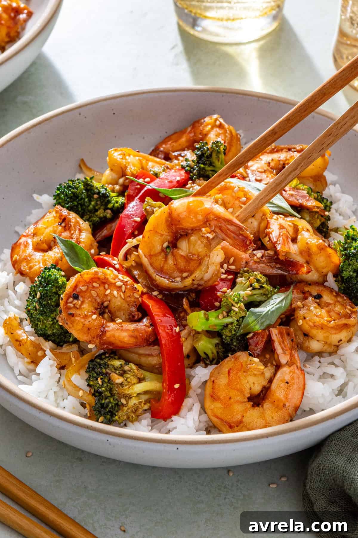Easy shrimp stir fry served over rice with chopsticks lifting shrimp from bowl