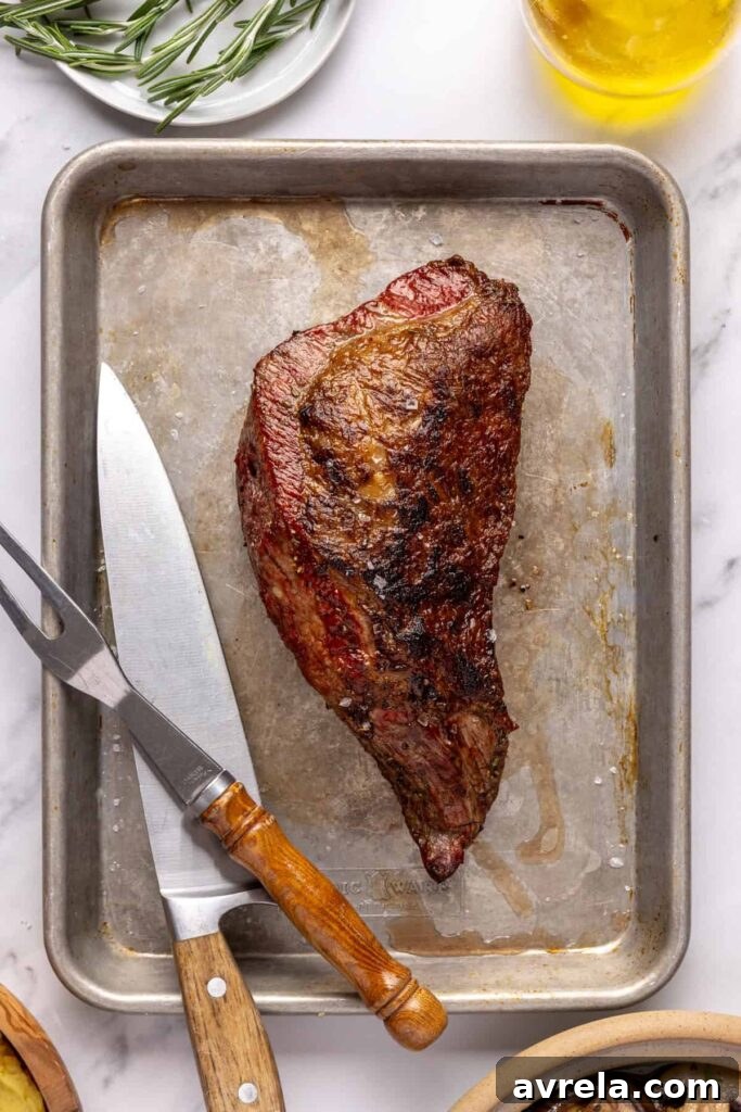 Juicy grass-fed tri-tip steak on a cutting board, seasoned with salt, pepper, and fresh rosemary