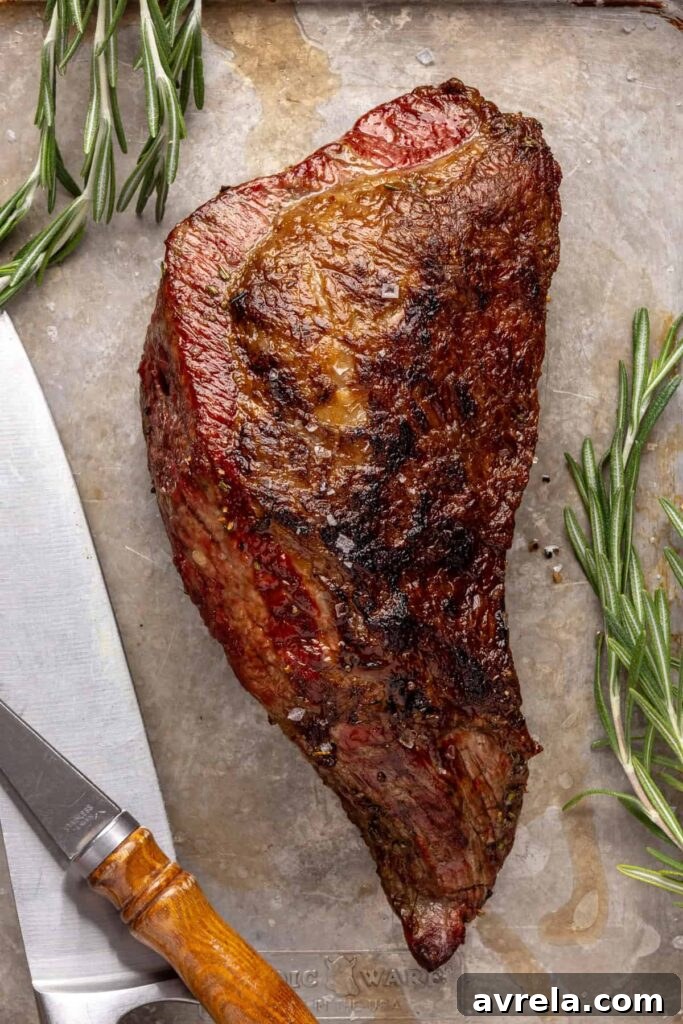 close-up of juicy grass-fed tri-tip steak on a cutting board, seasoned with salt, pepper, and fresh rosemary