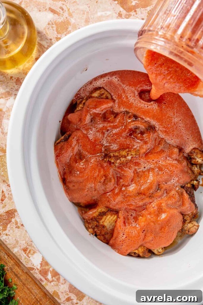 Chicken tinga cooking in a slow cooker with smoky tomato sauce
