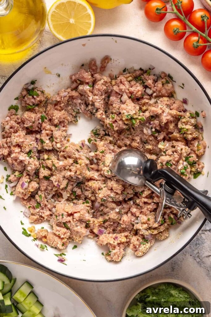Scooping ground turkey meatball mixture with herbs, garlic, and breadcrumbs in a bowl for Greek turkey meatballs.