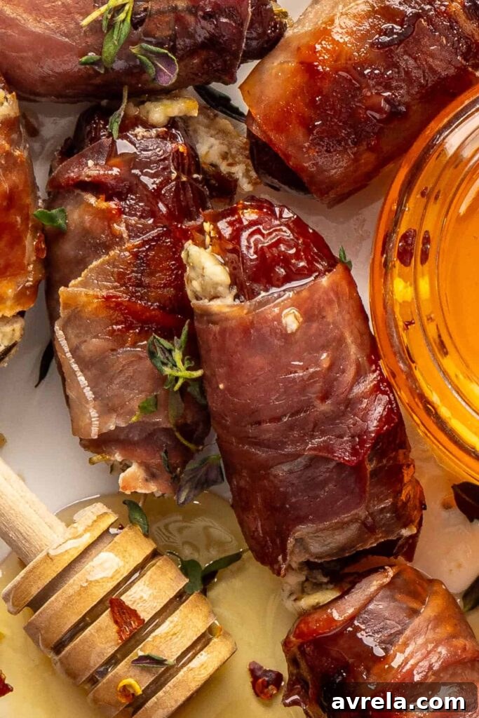 close-up overhead view of prosciutto wrapped stuffed dates with goat cheese and hot honey, next to a honey wand