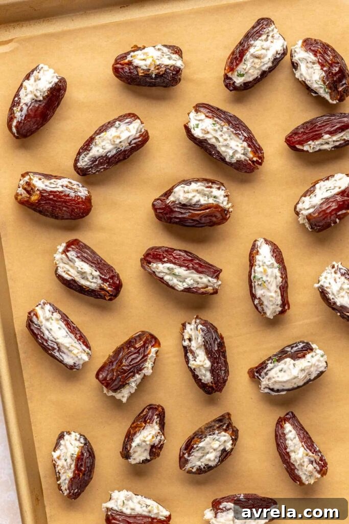 Medjool dates filled with herbed goat cheese, lemon zest, walnuts, and parsley, on a parchment paper-lined baking sheet, ready to be wrapped in prosciutto before baking
