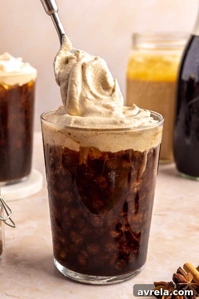 Dolloping pumpkin cold foam on top of a glass of iced coffee