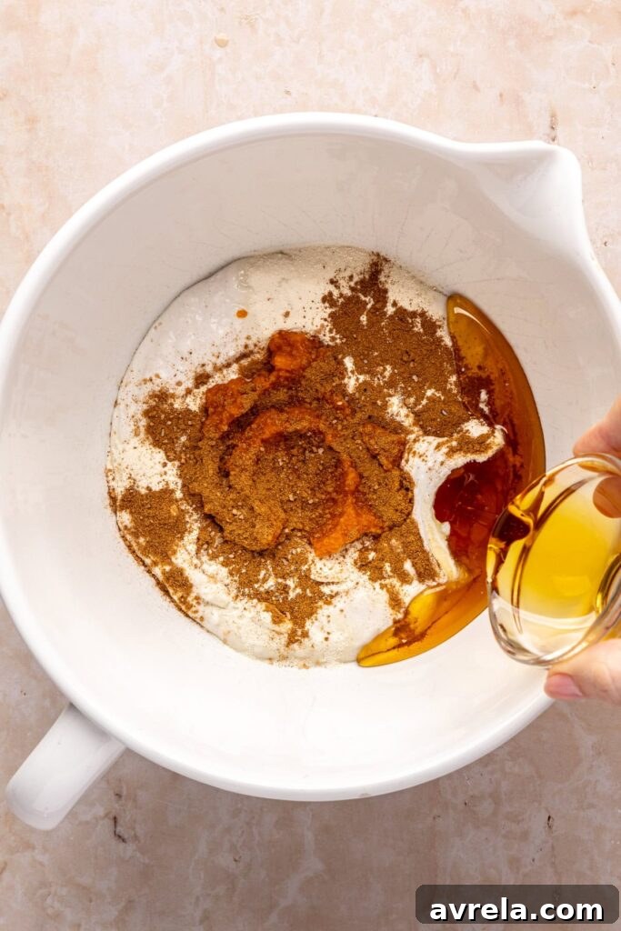 pouring maple syrup into a mixing bowl filled with ingredients to make homemade pumpkin cold foam