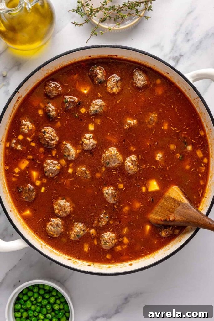 Stirring and simmering beef meatball soup with potatoes and fresh thyme in a Dutch oven