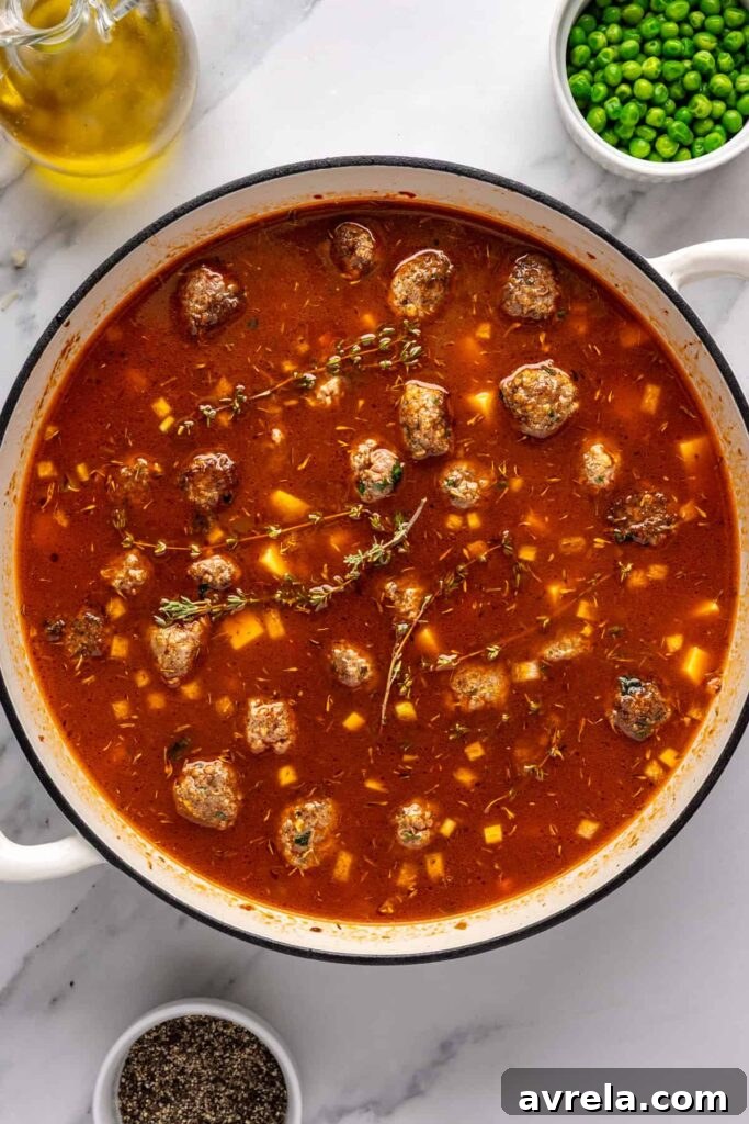 simmering beef meatball soup with potatoes and fresh thyme in a Dutch oven