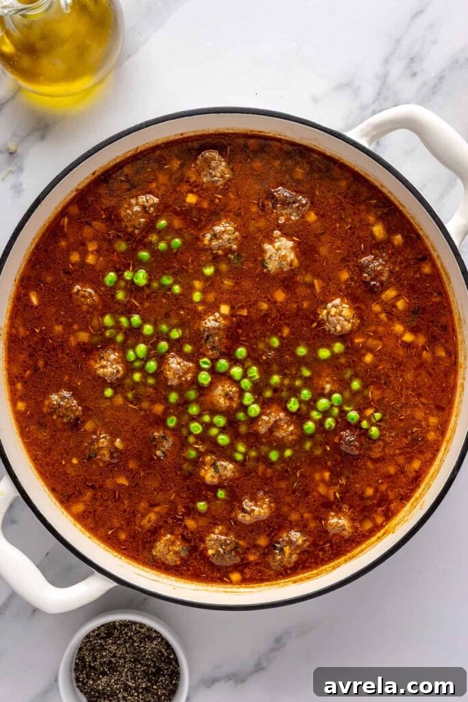 Finishing beef meatball soup by stirring in frozen peas