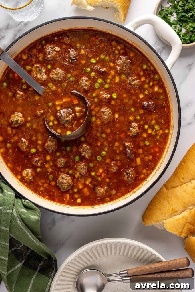 Overhead view of finished beef meatball soup in a Dutch oven with a soup ladle and a baguette on the side