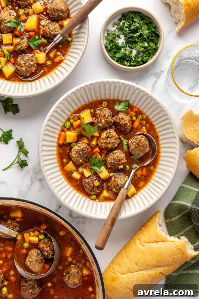 Overhead view of beef meatball soup served in a bowl with crusty baguette and on a table with garnishes