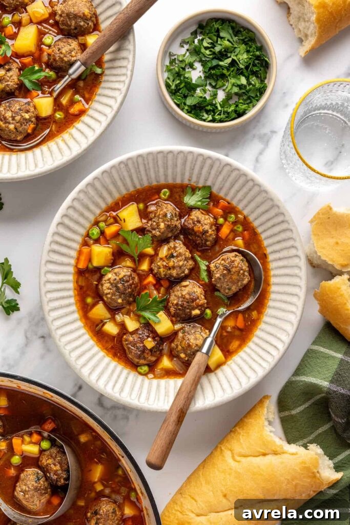 Overhead view of beef meatball soup served in a bowl with crusty baguette and on a table with garnishes