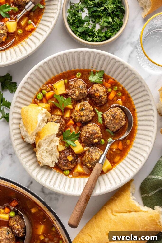 Overhead view of beef meatball soup served in a bowl with crusty baguette
