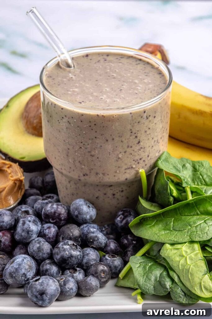Toddler Smoothie Recipes: Nutritious, Filling & Naturally Sweetened 12 Toddler smoothie in a glass on a table surrounded by fresh banana, blueberries, spinach, peanut butter, and avocado