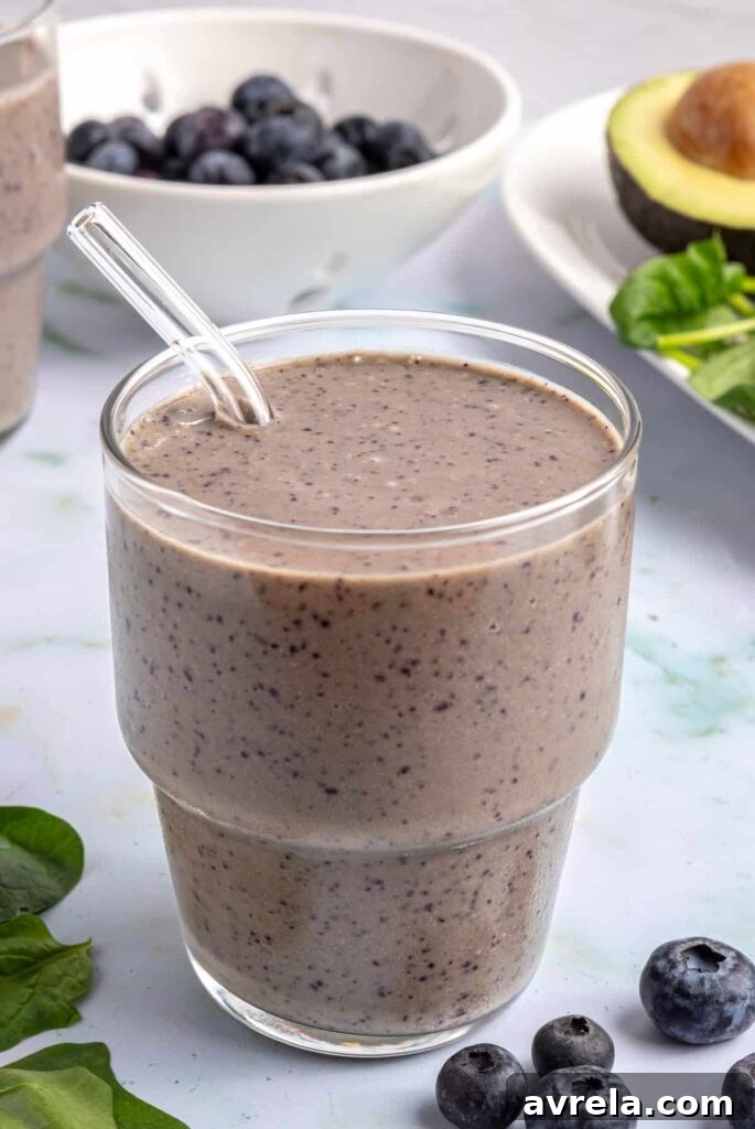 Toddler Smoothie Recipes: Nutritious, Filling & Naturally Sweetened 13 Toddler smoothie served in a glass with a reusable glass straw, on a table styled with blueberries and other ingredients nearby