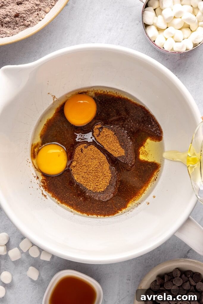 pouring avocado oil into the wet ingredients for hot cocoa cookies, including eggs, coconut sugar, in a large mixing bowl