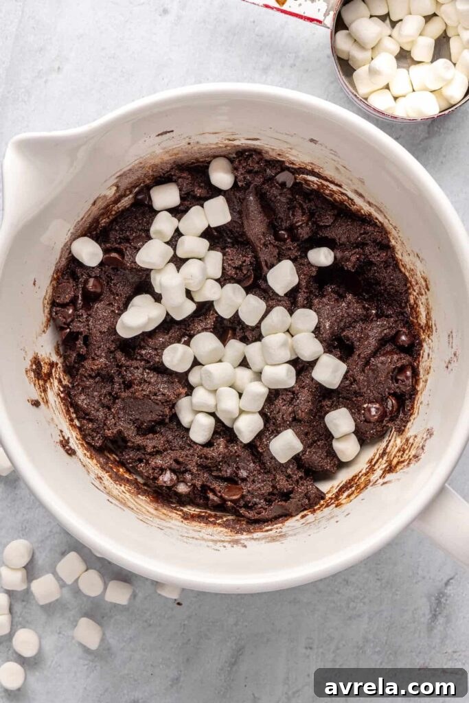 mini marshmallows in a large mixing bowl on top of hot cocoa cookie dough, ready to be folded in