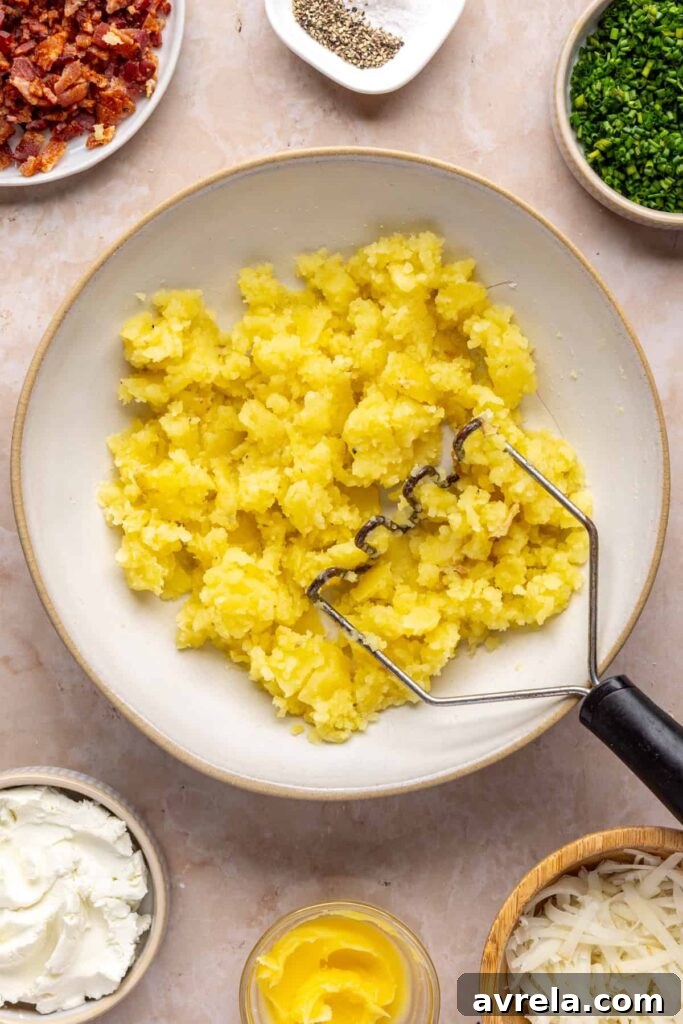 Mashed potato flesh in a bowl, before adding goat cheese, ghee, bacon, and chives to create the filling