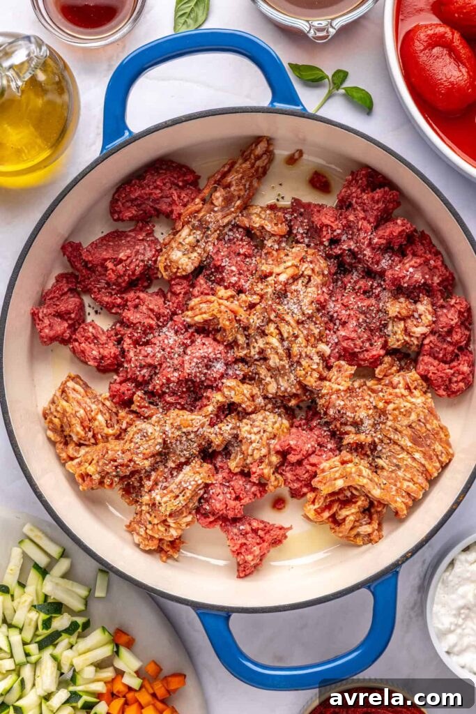 Overhead shot of ground beef and Italian sausage browning in a Dutch oven for creamy homemade vodka sauce