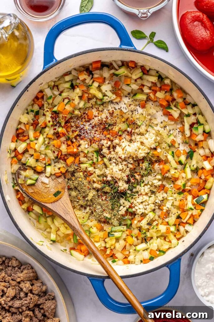 Vegetables cooking down in a Dutch oven, with seasonings being stirred in, for creamy vodka sauce with hidden veggies