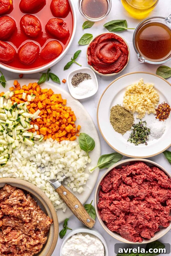 Overhead shot of ingredients for creamy homemade vodka sauce with hidden veggies, including tomatoes, onion, zucchini, carrot, garlic, and herbs