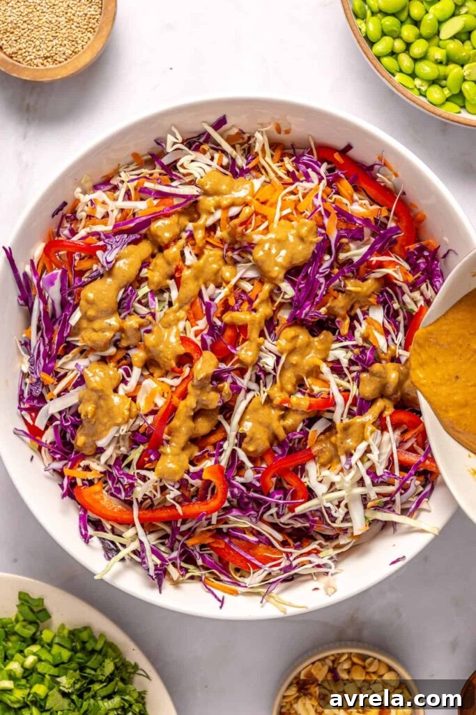 pouring peanut dressing over top bowl of fresh vegetables for crunchy peanut cabbage salad