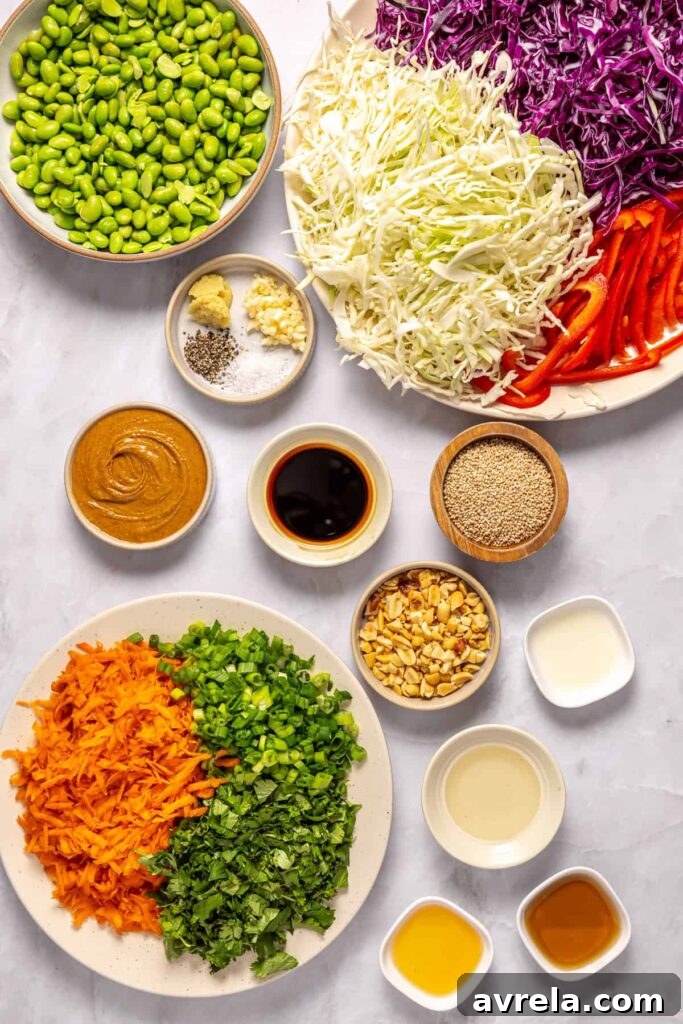 Overhead shot of ingredients for crunchy peanut cabbage salad including green cabbage, red cabbage, carrots, edamame, peanut butter, and sesame oil