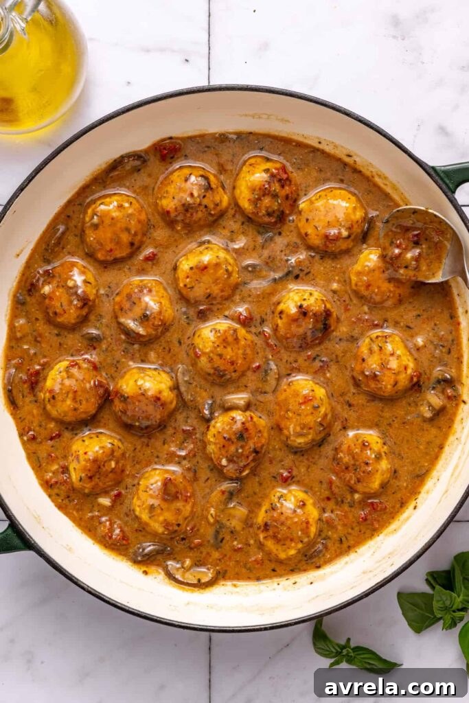 Adding chicken meatballs back into skillet with creamy sauce before baking