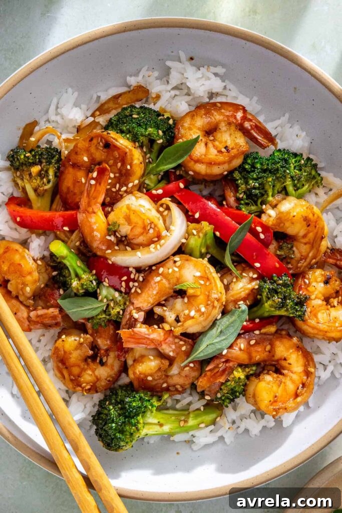Overhead shrimp stir fry bowl with rice, sesame seeds, and basil
