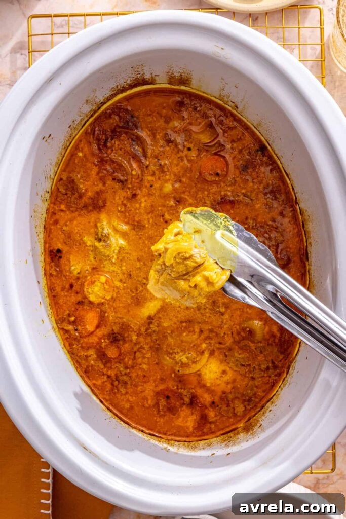 Slow Cooker Coconut Chicken Curry Recipe for Tender, Flavorful Meals 11 tongs removing chicken from slow cooker chicken curry, before shredding