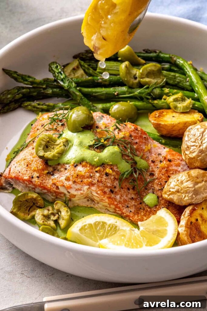 Roasted lemon being squeezed over baked salmon and asparagus