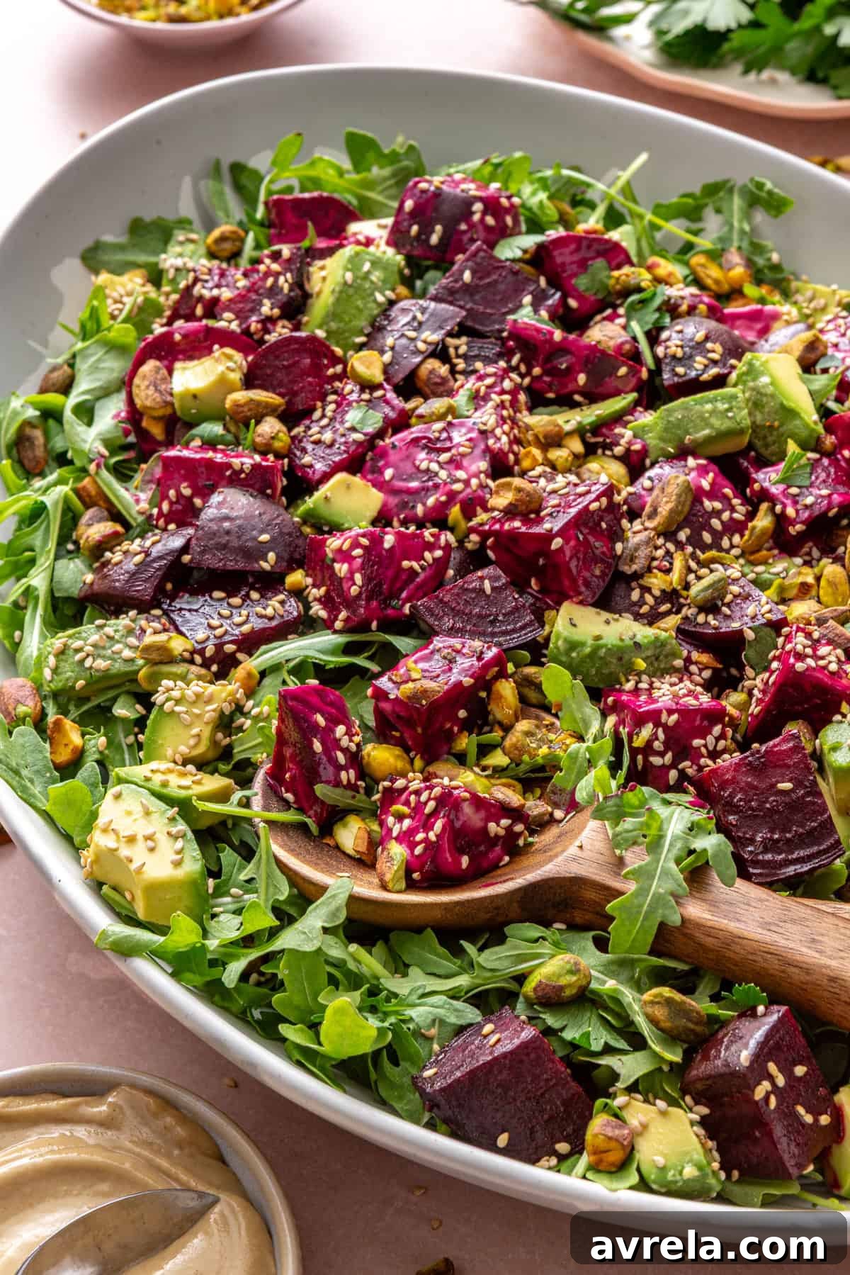 Roasted beet salad with goat cheese, avocado, arugula, pistachios, and tahini dressing served in a platter with a serving spoon on a styled table