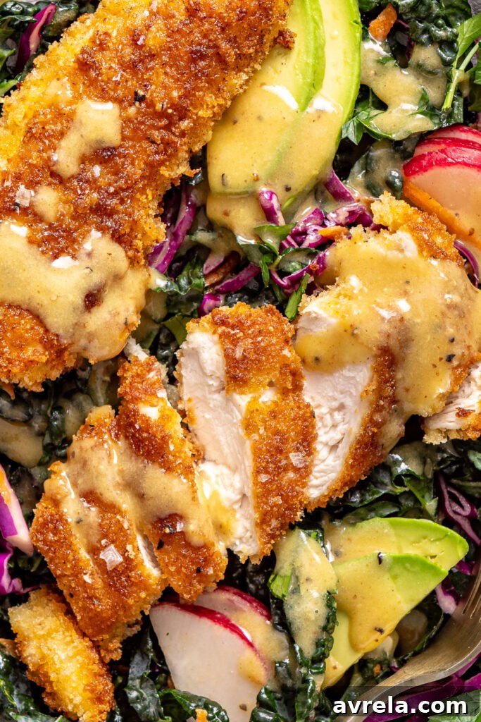 Close-up detail of sliced crispy chicken on kale salad with avocado